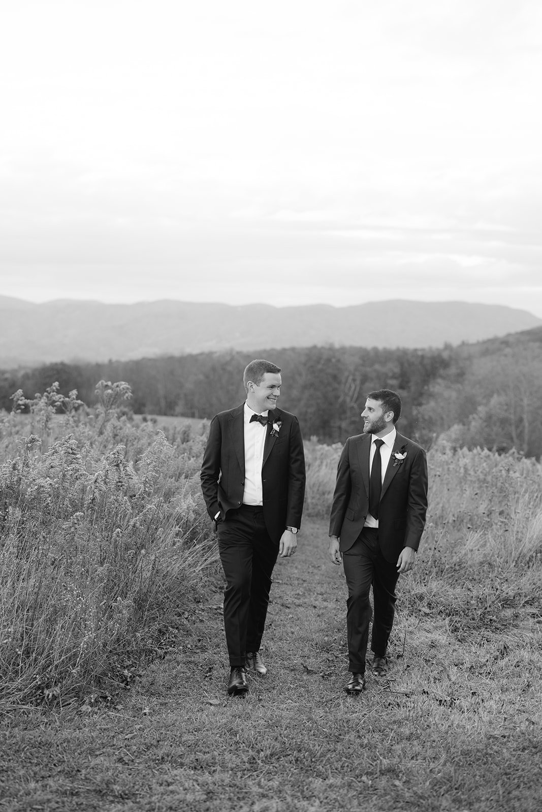 Two grooms walking through a field in the blue ridge mountains.
