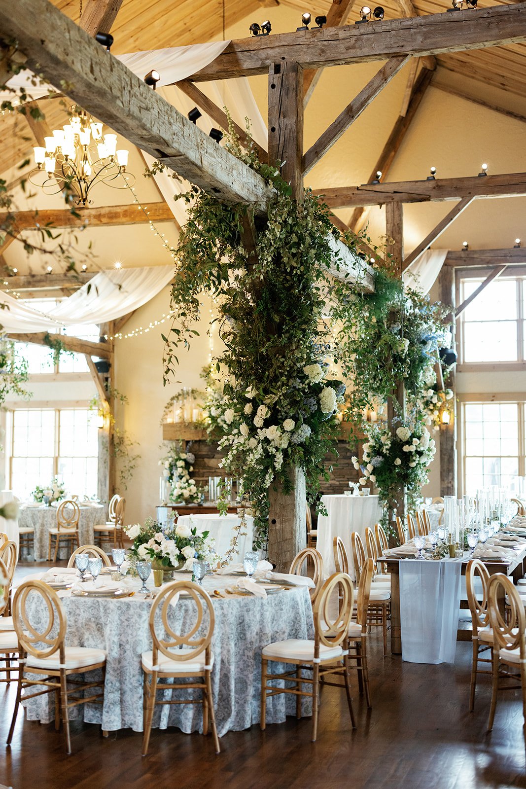 A wedding venue with wooden beams adorned with greenery and tables with blue and white linens. 